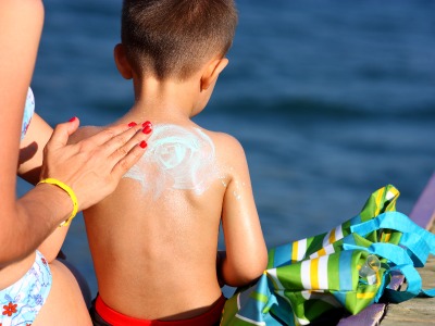 A person applying sunscreen to a child’s back.